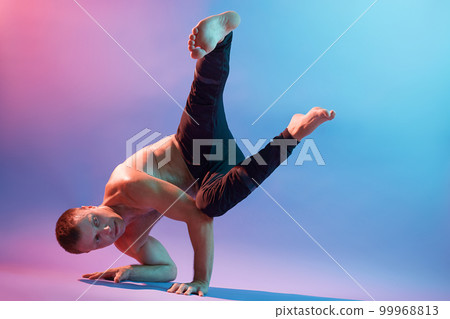 Strong flexible man doing morning yoga exercises isolated over neon wall, wearing black pants, looks serious and concentrated, practicing body balance. Strong flexible man doing morning yoga exercises isolated over neon wall, wearing black pants, looks serious and concentrated, practicing body balance. 99968813