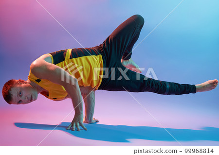Young man doing an asana, standing on hands, practicing body balance, wearing sports wears, doing yoga exercises isolated over neon wall, sportsman working out. Young man doing an asana, standing on hands, practicing body balance, wearing sports wears, doing yoga exercises isolated over neon wall, sportsman working out. 99968814