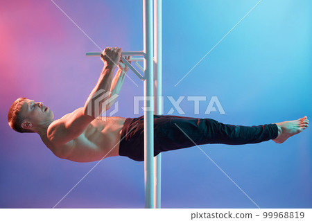 Handsome muscular man doing exercises on horizontal bar indoors isolated over neon background. Calisthenics workout, topless guy wearing black trousers. Handsome muscular man doing exercises on horizontal bar indoors isolated over neon background. Calisthenics workout, topless guy wearing black trousers. 99968819