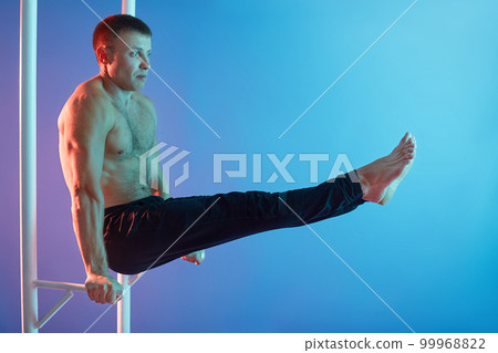 Handsome young man exercising on horizontal bar against neon wall, doing abs exercises topless isolated over neon background, has perfect sport shape. Handsome young man exercising on horizontal bar against neon wall, doing abs exercises topless isolated over neon background, has perfect sport shape. 99968822
