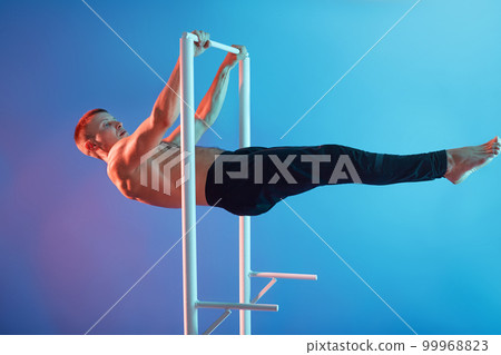 Athlete man training at horizontal bar, posing barefoot and topless, wearing black pants, guy working out on crossbar, handsome sportsman doing sports. 99968823