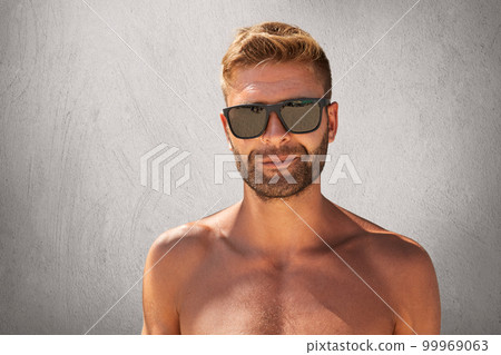 Young bodybuilder with trendy hairstyle, bristle, wearing sunglasses, standing naked over grey background. Stylish unshaven man with beautiful muscular body, isolated. People, beauty concept Young bodybuilder with trendy hairstyle, bristle, wearing sunglasses, standing naked over grey background. Stylish unshaven man with beautiful muscular body, isolated. People, beauty concept 99969063