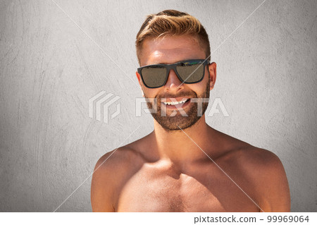 Handsome tanned man with trendy hairdo, bristle, standing topless, demonstrating his muscular body, wearing sunglasses, having pleasant smile, showing his perfect white teeth. Glad sportsman Handsome tanned man with trendy hairdo, bristle, standing topless, demonstrating his muscular body, wearing sunglasses, having pleasant smile, showing his perfect white teeth. Glad sportsman 99969064