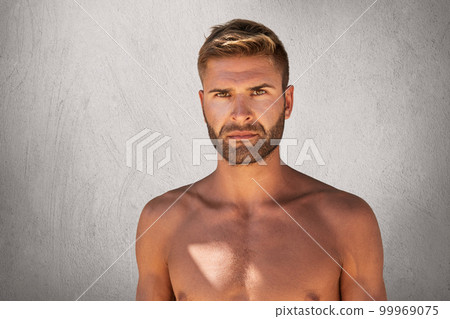 Muscular guy with bare torso looking confidently into camera being isolated over grey concrete wall. Handsome unshaven male with dark eyes and trendy hairstyle being naked. Human body and sport Muscular guy with bare torso looking confidently into camera being isolated over grey concrete wall. Handsome unshaven male with dark eyes and trendy hairstyle being naked. Human body and sport 99969075