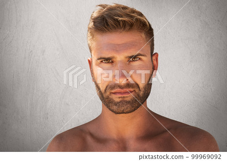 Close up portrait of pleasant-looking man with dark eyes, stylish hairdo, bristle and tanned skin looking seriously into camera while scowling his eyebrows. Strong young man with confident look Close up portrait of pleasant-looking man with dark eyes, stylish hairdo, bristle and tanned skin looking seriously into camera while scowling his eyebrows. Strong young man with confident look 99969092