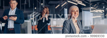 Smiling muslim businesswoman in hijab working on computer while sitting in modern office 99969330