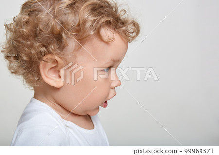 Adorable blonde baby looking at something with interest and opened mouth, side view of curious infant , copy space for advertisement for promotional text. Adorable blonde baby looking at something with interest and opened mouth, side view of curious infant , copy space for advertisement for promotional text. 99969371