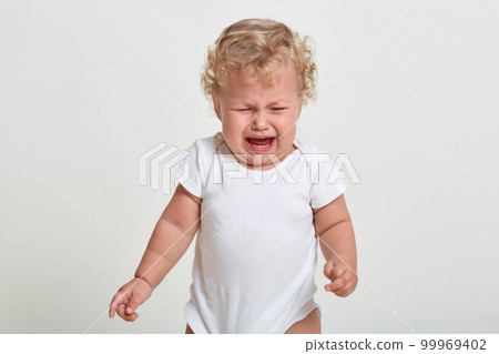 Portrait of sad upset little boy crying, looking down, frowning face, wearing bodysuit, being in bed mood, feels hungry, posing isolated over white background. 99969402