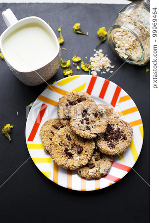 Oatmeal cookies with chocolate on a plate with colorful cup milk. 99969464