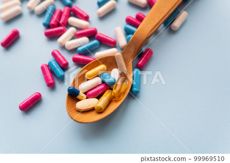 Various bright pills on a blue background lie in a wooden spoon against the background of different bright pills. Health care concept, close-up. 99969510