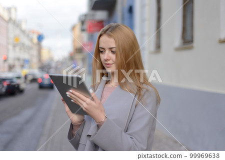 girl with red hair in coat looks something in a tablet on a city 99969638