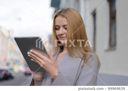 girl with red hair in coat looks something in a tablet on a city 99969639