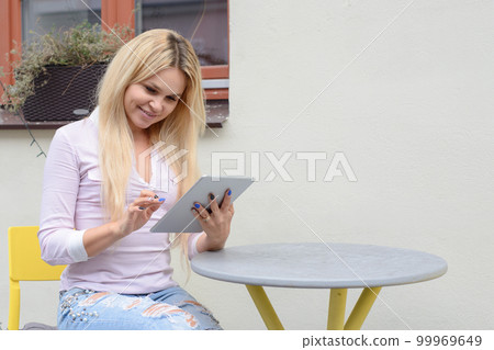 blond girl sitting at a table near a cafe, looking for something 99969649