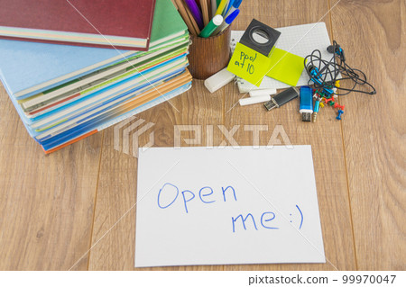 student desktop, books, accessories, stationery. in the foreground is an envelope bearing the words " open me" student desktop, books, accessories, stationery. in the foreground is an envelope bearing the words " open me" 99970047