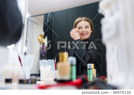 Woman applying powder while making up in a backstage Woman applying powder while making up in a backstage 99970130
