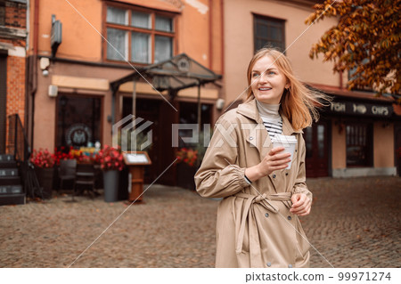 Charming 20s woman drinks coffee. Smile girl spend free time traveling in European old town enjoying cup of tea, coffee. Gdansk, Poland 99971274