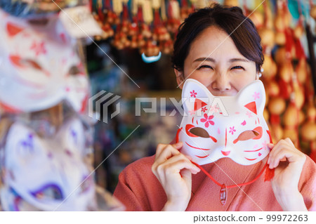 A woman in a kimono with a fox mask at a souvenir shop in Kyoto 99972263