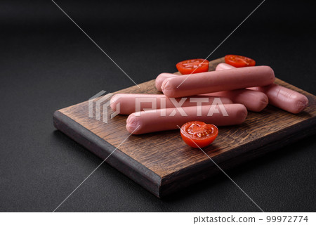 Boiled sausages on a wooden cutting board with tomatoes, spices and salt 99972774