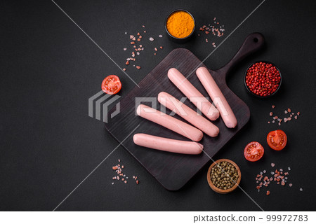 Boiled sausages on a wooden cutting board with tomatoes, spices and salt 99972783