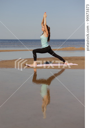 yoga, Warrior Pose, sporty woman does a warm-up on seashore in morning. yoga, Warrior Pose, sporty woman does a warm-up on seashore in morning. 99973873