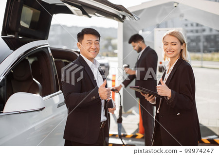 Multiracial colleagues standing at station and charging EV Multiracial colleagues standing at station and charging EV 99974247