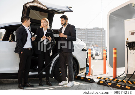 Multiracial businesspeople refilling EV at charging location 99974258