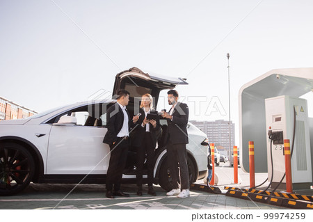 Multiracial businesspeople refilling EV at charging location 99974259