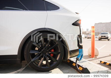 Modern electric car charging at outdoors EV station 99974309