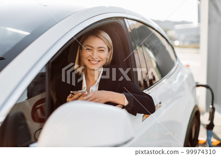 Woman working on smartphone while charging electric car 99974310