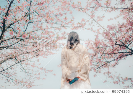 Photo of a woman standing with a smartphone against a cherry blossom background 99974395