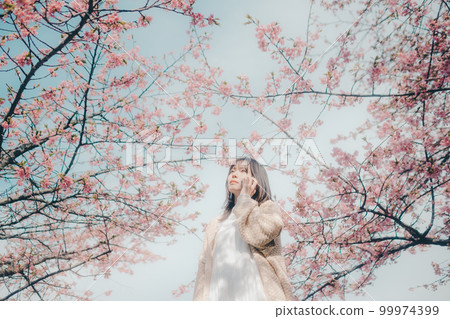 Photo of a woman standing with a smartphone against a cherry blossom background Photo of a woman standing with a smartphone against a cherry blossom background 99974399
