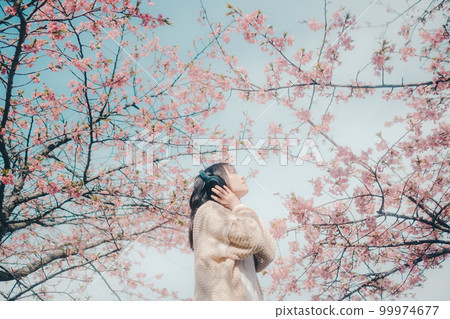 Photo of a woman listening to music with a cherry blossom background 99974677