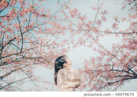 Photo of a woman listening to music with a cherry blossom background 99974679