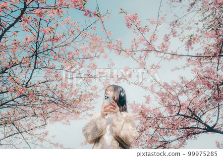 Photo of a woman listening to music with a cherry blossom background 99975285