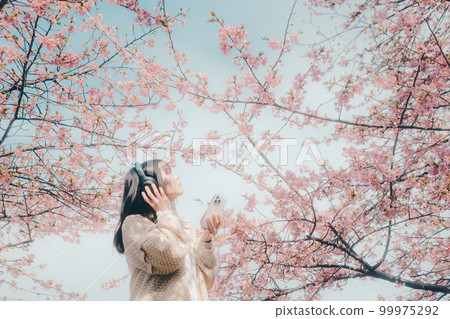 Photo of a woman listening to music with a cherry blossom background 99975292