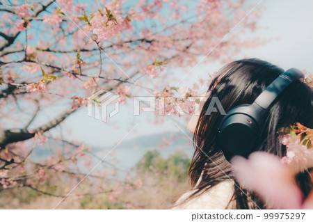 Photo of a woman listening to music with a cherry blossom background Photo of a woman listening to music with a cherry blossom background 99975297