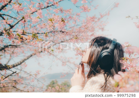 Photo of a woman listening to music with a cherry blossom background 99975298