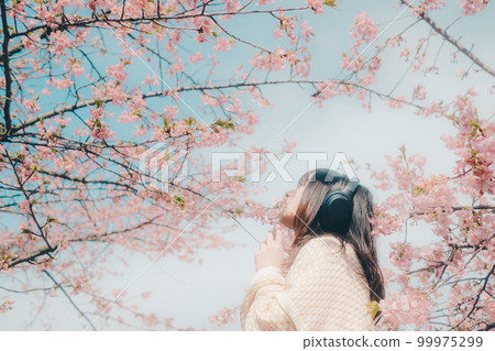 Photo of a woman listening to music with a cherry blossom background 99975299