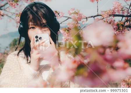 Photo of a woman listening to music with a cherry blossom background 99975301