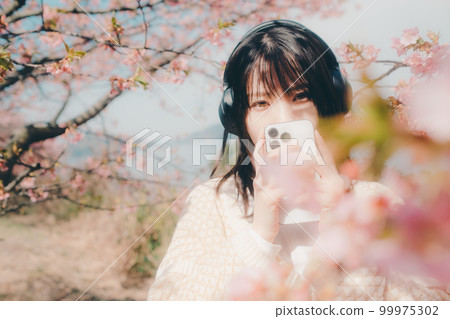 Photo of a woman listening to music with a cherry blossom background 99975302