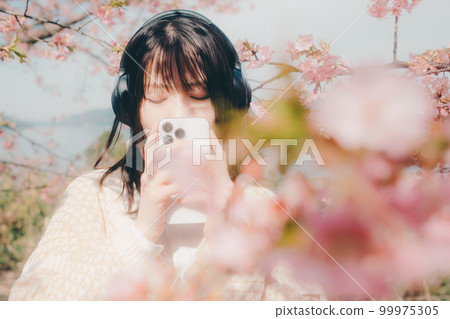 Photo of a woman listening to music with a cherry blossom background 99975305