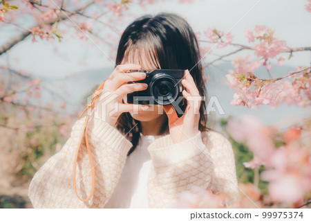 Photo of a woman holding a mirrorless camera with a cherry blossom background Photo of a woman holding a mirrorless camera with a cherry blossom background 99975374