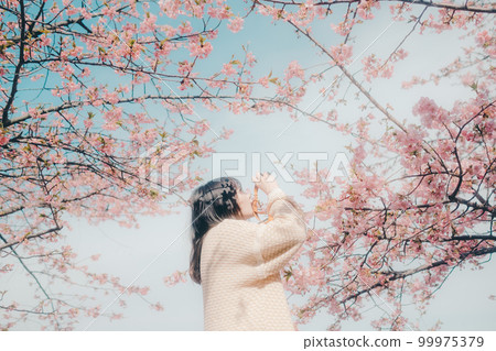 Photo of a woman holding a mirrorless camera with a cherry blossom background 99975379