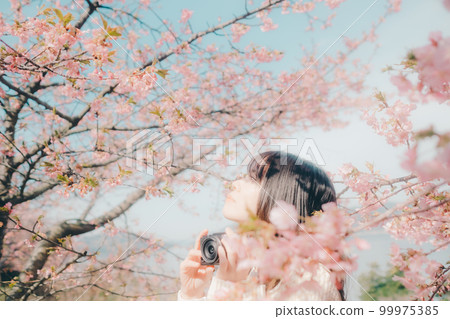 Photo of a woman holding a mirrorless camera with a cherry blossom background Photo of a woman holding a mirrorless camera with a cherry blossom background 99975385