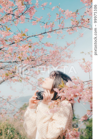 Photo of a woman holding a mirrorless camera with a cherry blossom background Photo of a woman holding a mirrorless camera with a cherry blossom background 99975386