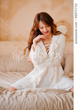 a beautiful woman in a white sexy dress with lacing and ruffles in bed a beautiful woman in a white sexy dress with lacing and ruffles in bed 99975710