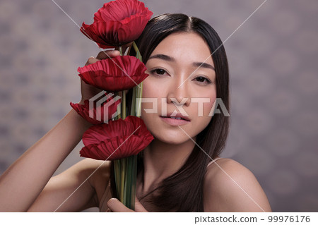 Asian young woman leaning red poppies to face portrait. Attractive lady holding romantic love symbol in hands, looking at camera and posing with beautiful bright flowers bouquet Asian young woman leaning red poppies to face portrait. Attractive lady holding romantic love symbol in hands, looking at camera and posing with beautiful bright flowers bouquet 99976176