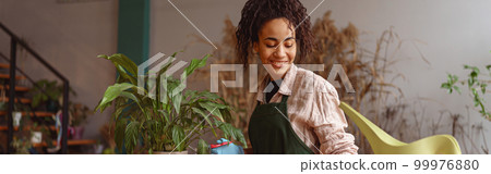 Smiling woman florist taking care of plant watering it in floral shop 99976880