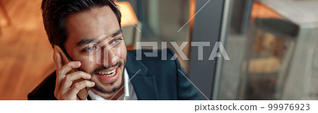 Happy indian businessman is talking phone with client during lunch time in cozy cafe Happy indian businessman is talking phone with client during lunch time in cozy cafe 99976923