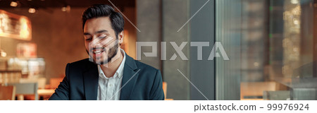 Smiling businessman working with graphs and charts at modern cafe Smiling businessman working with graphs and charts at modern cafe 99976924